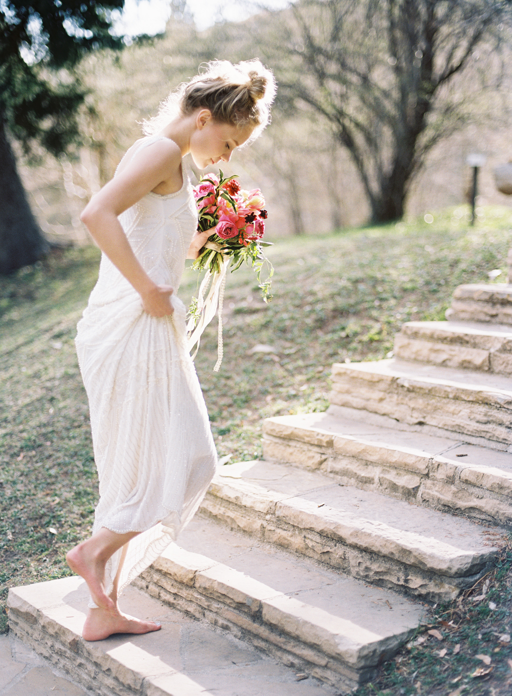 a film photograph of a bride walking through memorial park in salt lake city on her wedding day holding a bouquet by ashley beyer of tinge