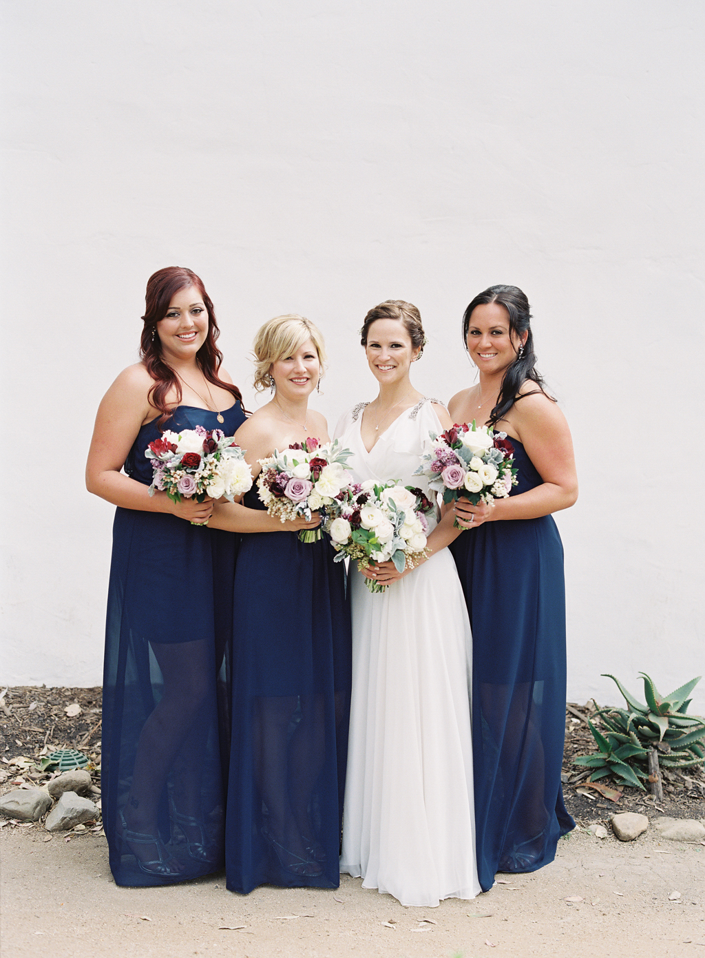 bride and her bridesmaids in front of a white background with bouquets by art with nature from orange county