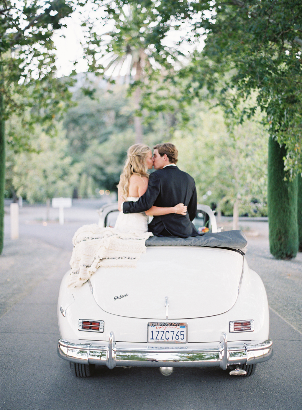 bride and groom kissing on their wedding day with vintage car shot using fuji 400h film