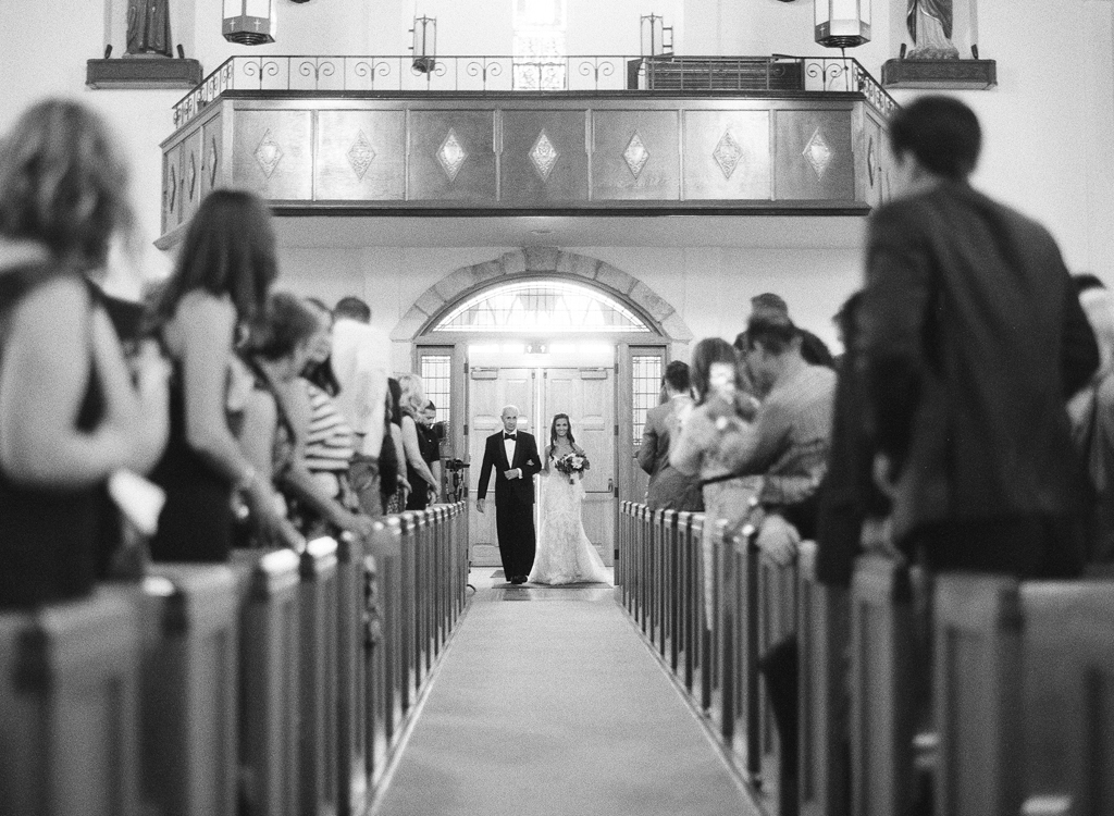 a black and white photo of a bride and her father walking down the aisle during her wedding ceremony. 
